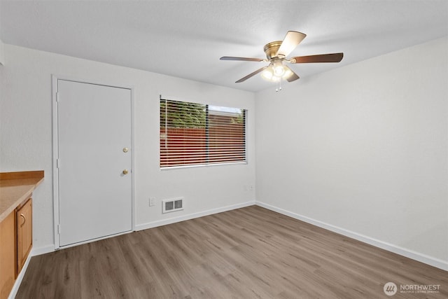 unfurnished room with light wood-type flooring, visible vents, ceiling fan, and baseboards