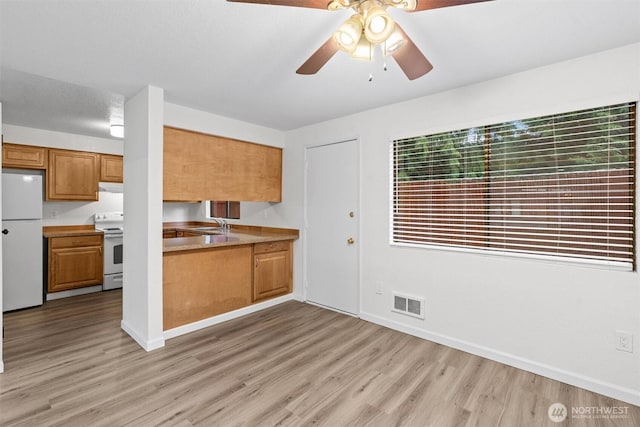 kitchen featuring brown cabinets, light countertops, visible vents, light wood-style flooring, and white appliances