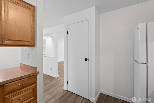 kitchen featuring brown cabinets, light countertops, freestanding refrigerator, wood finished floors, and baseboards