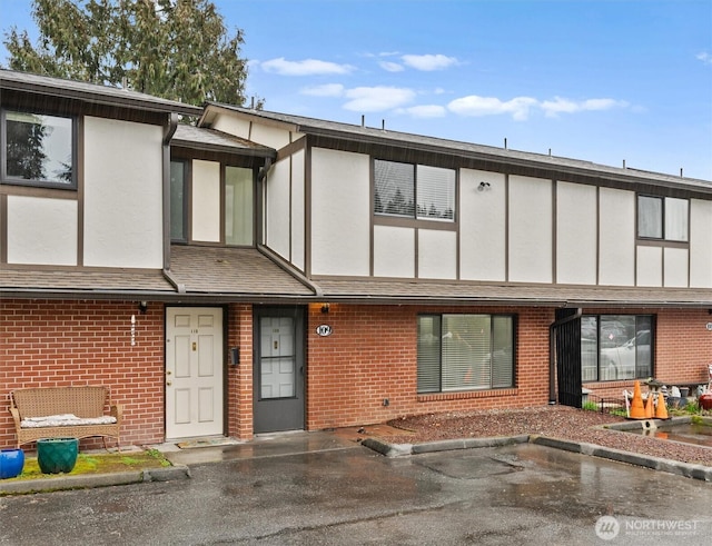 multi unit property with brick siding, a shingled roof, uncovered parking, and stucco siding