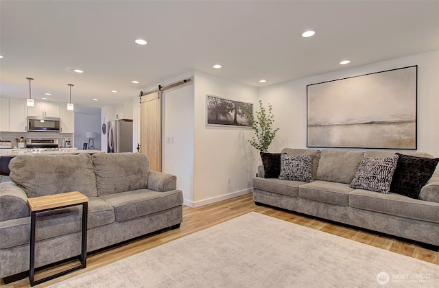 living room with a barn door, light wood-style flooring, recessed lighting, and baseboards