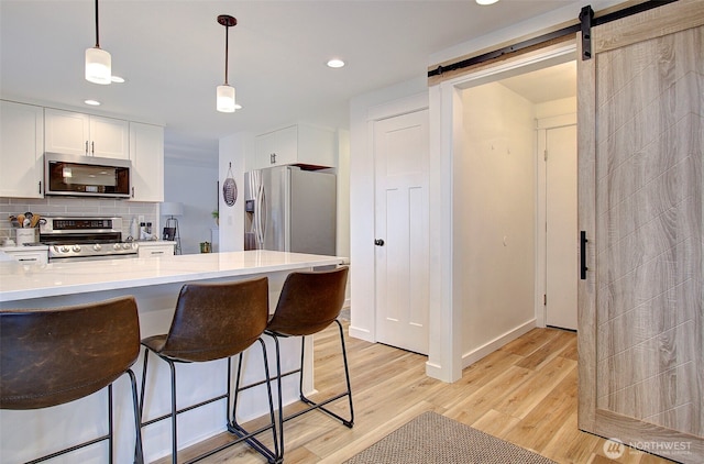 kitchen featuring stainless steel appliances, white cabinets, light wood-style floors, a barn door, and backsplash