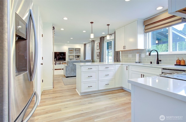 kitchen featuring a sink, white cabinetry, stainless steel fridge, a peninsula, and light wood finished floors