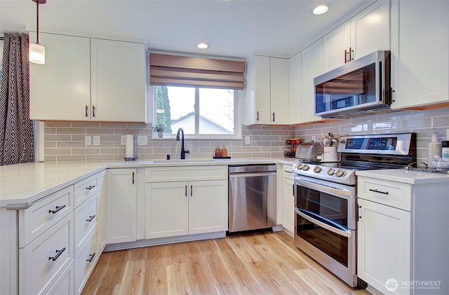 kitchen with appliances with stainless steel finishes, white cabinetry, light wood-style floors, and a sink