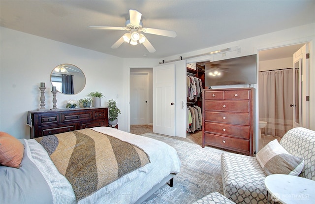 bedroom with ceiling fan, a spacious closet, a closet, light carpet, and a barn door