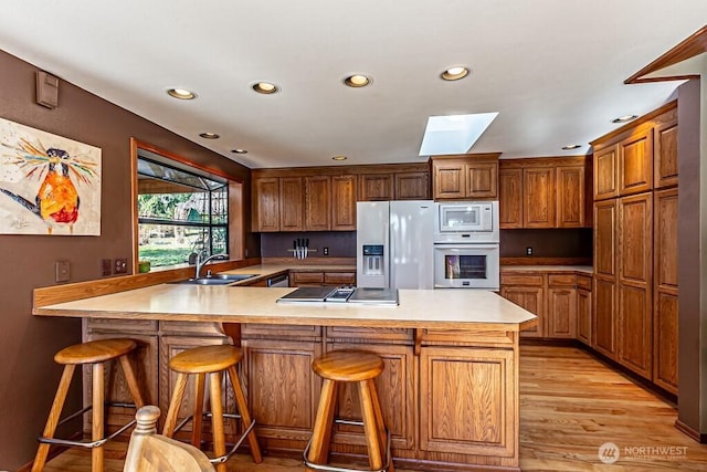 kitchen with a peninsula, white appliances, a skylight, a sink, and light countertops