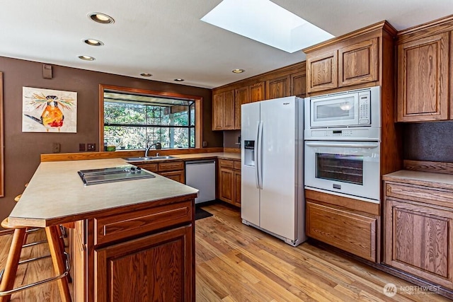 kitchen with a skylight, light wood-style floors, a sink, white appliances, and a peninsula