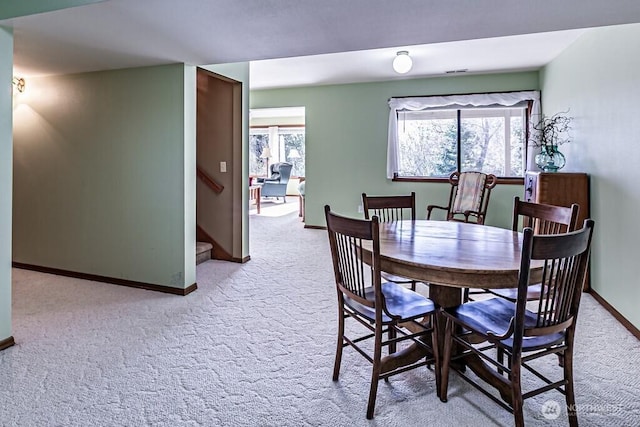 dining space featuring light carpet, stairs, and baseboards