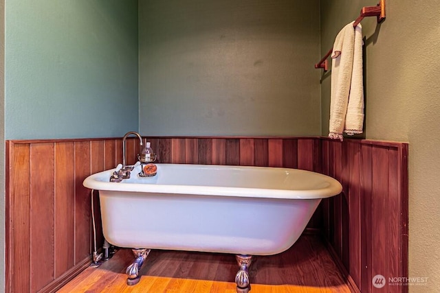 bathroom with wainscoting, a soaking tub, and wood finished floors