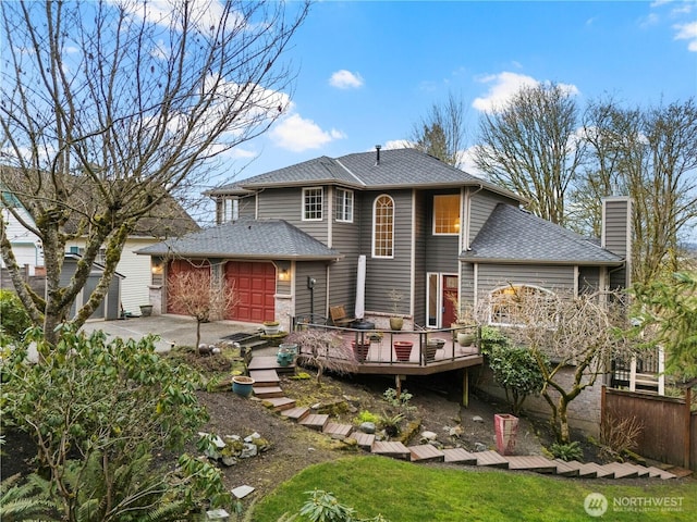 rear view of property with roof with shingles, a yard, a chimney, a garage, and a wooden deck