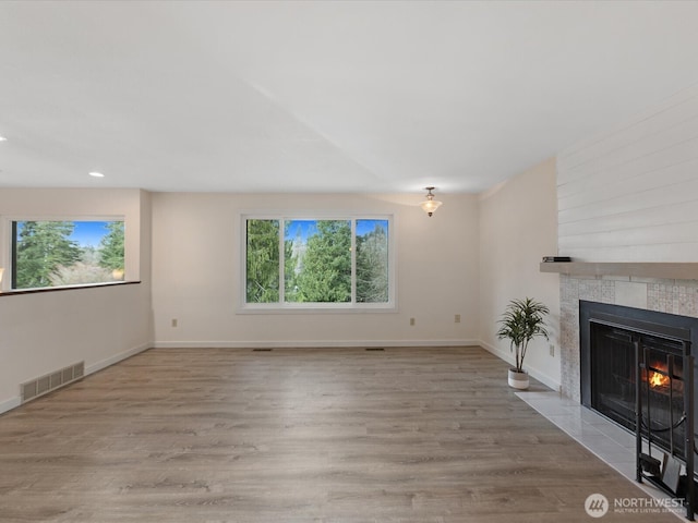 unfurnished living room featuring a wealth of natural light, visible vents, a tiled fireplace, and wood finished floors