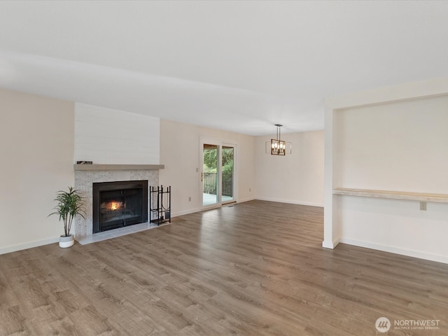 unfurnished living room featuring an inviting chandelier, a fireplace with flush hearth, baseboards, and wood finished floors