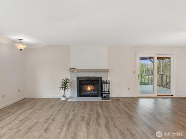 unfurnished living room featuring a tiled fireplace, wood finished floors, and baseboards