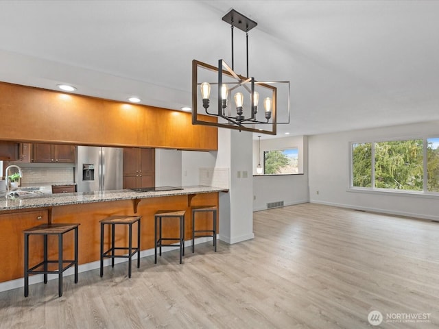 kitchen featuring brown cabinets, visible vents, a chandelier, stainless steel fridge with ice dispenser, and black electric cooktop