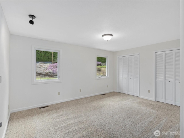 unfurnished bedroom with carpet floors, two closets, visible vents, and baseboards