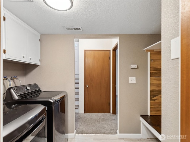 washroom with a textured ceiling, visible vents, baseboards, washer and dryer, and cabinet space