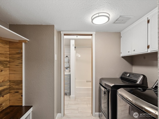 laundry room featuring cabinet space, a textured wall, visible vents, washing machine and dryer, and a textured ceiling