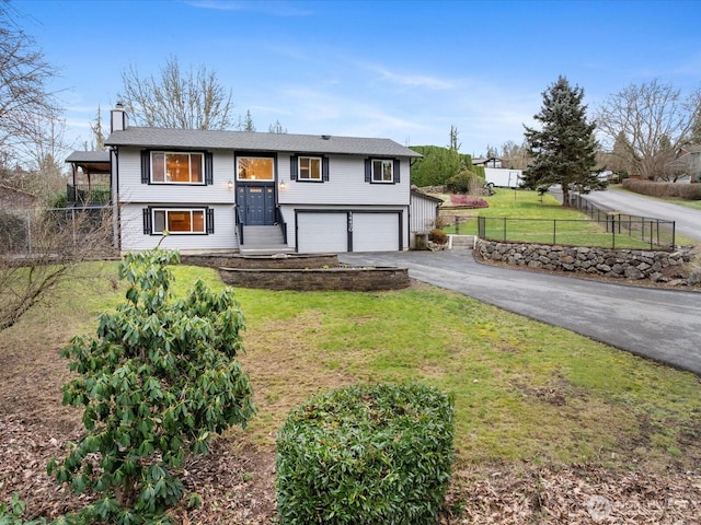 bi-level home featuring aphalt driveway, a chimney, a front yard, fence, and a garage