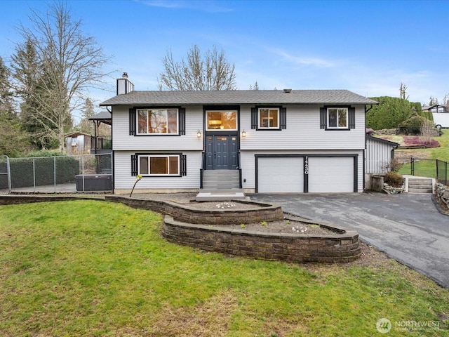 bi-level home featuring driveway, a garage, a chimney, fence, and a front yard