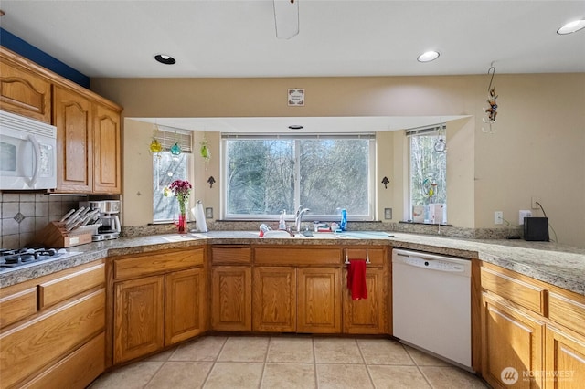 kitchen with tile counters, light tile patterned floors, brown cabinetry, white appliances, and a sink