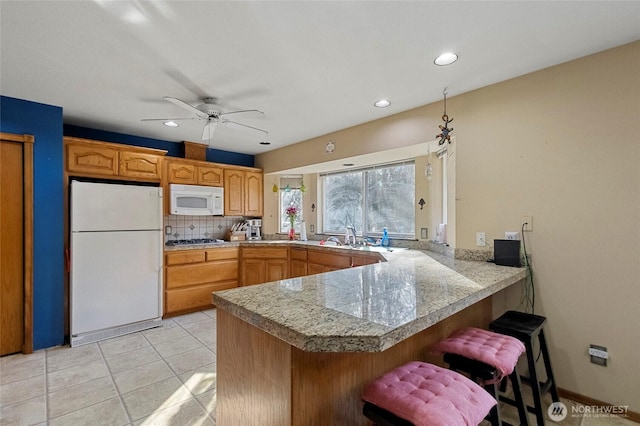 kitchen featuring a kitchen breakfast bar, white appliances, a peninsula, decorative backsplash, and tile counters