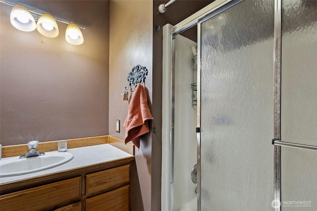 full bathroom featuring a shower with shower door, vanity, and a textured wall