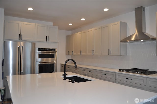 kitchen with stainless steel appliances, light countertops, backsplash, a sink, and wall chimney exhaust hood