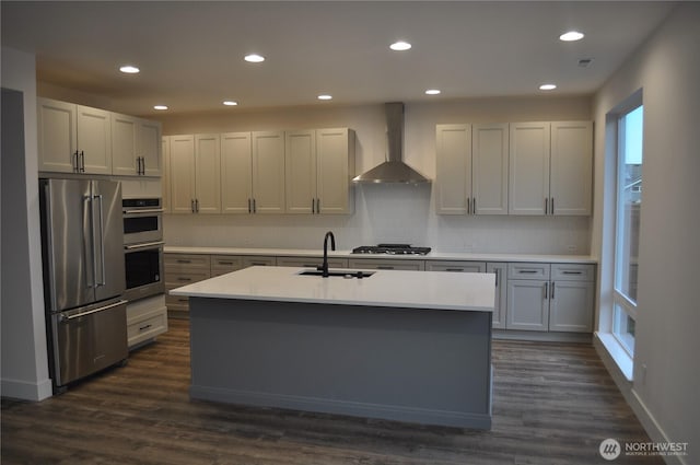 kitchen with dark wood-style floors, light countertops, appliances with stainless steel finishes, a sink, and wall chimney exhaust hood