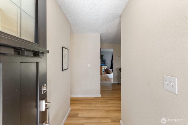 hallway with baseboards, light wood-style floors, and a textured ceiling