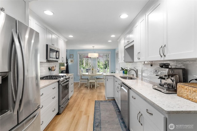 kitchen featuring light wood finished floors, white cabinets, stainless steel appliances, and a sink