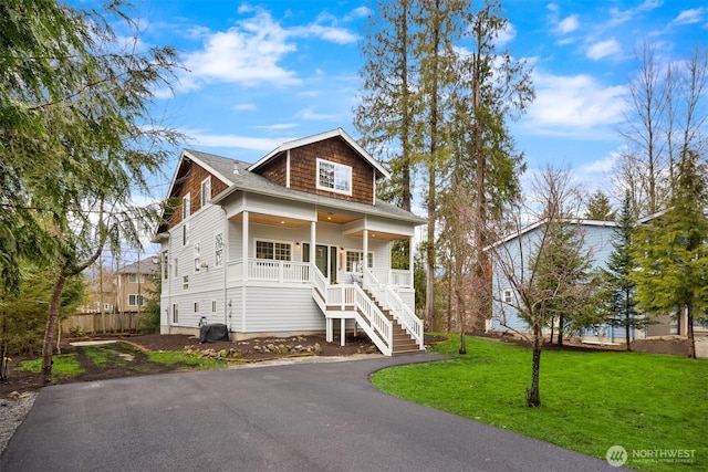 view of front of property featuring a front lawn, stairway, covered porch, and aphalt driveway