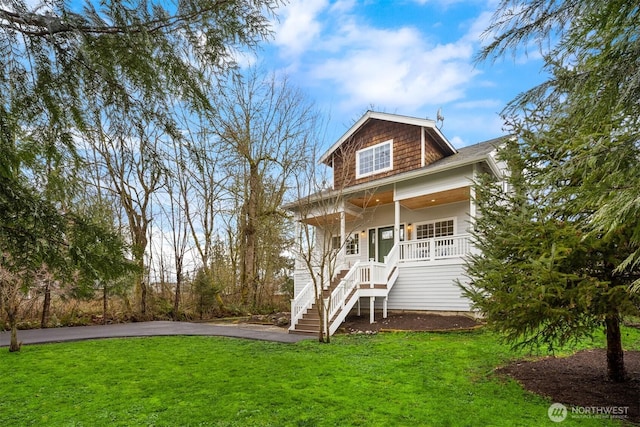 view of front of home with stairs, driveway, covered porch, and a front yard