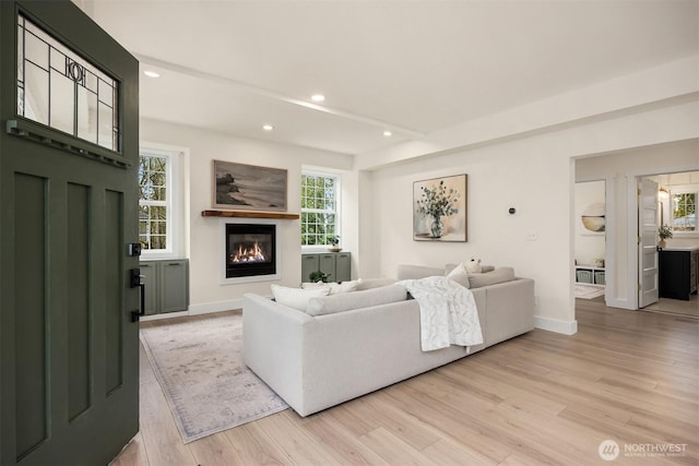 living area featuring a glass covered fireplace, recessed lighting, light wood-type flooring, and baseboards