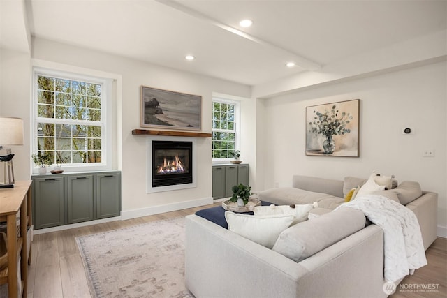 living area with recessed lighting, baseboards, light wood-style floors, and a glass covered fireplace