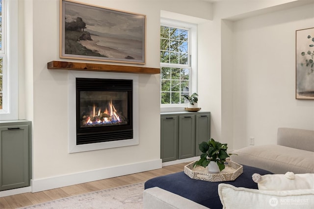 sitting room with a glass covered fireplace, baseboards, and light wood-style floors