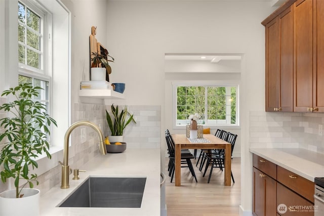 kitchen with light wood-type flooring, light countertops, decorative backsplash, brown cabinets, and a sink