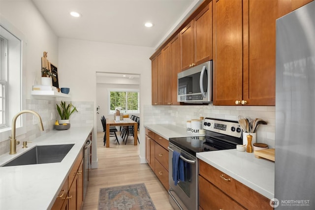 kitchen with light wood-type flooring, brown cabinets, a sink, stainless steel appliances, and light countertops