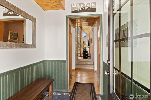 hall featuring a wainscoted wall, wood ceiling, wood finished floors, and beamed ceiling