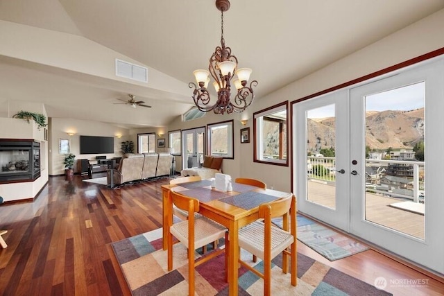 dining room featuring french doors, visible vents, vaulted ceiling, wood finished floors, and a multi sided fireplace