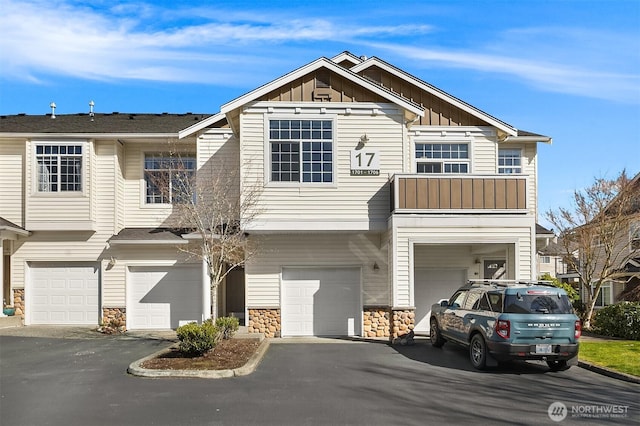 townhome / multi-family property with stone siding, board and batten siding, an attached garage, and driveway