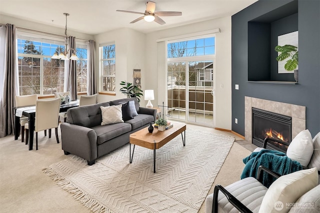 living area featuring baseboards, light colored carpet, ceiling fan with notable chandelier, and a tile fireplace