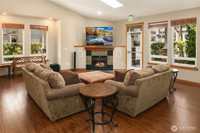 living room with lofted ceiling with skylight, dark wood-type flooring, a healthy amount of sunlight, and a tile fireplace