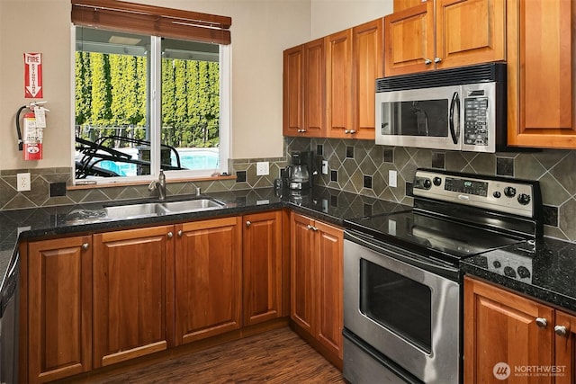 kitchen with dark wood-type flooring, decorative backsplash, brown cabinets, appliances with stainless steel finishes, and a sink