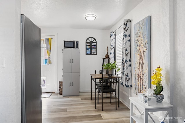 dining area with a textured wall, baseboards, light wood finished floors, and a textured ceiling