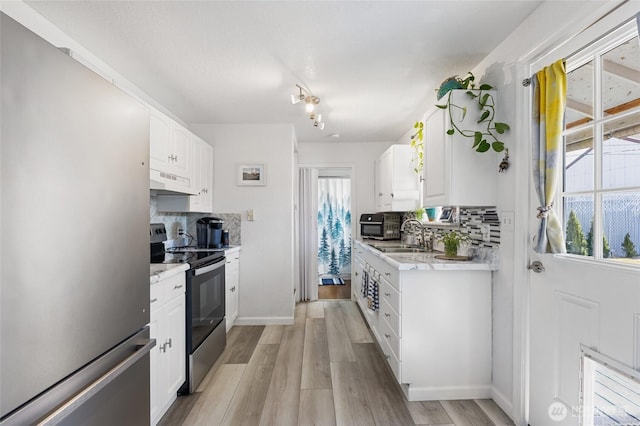 kitchen featuring light wood finished floors, a sink, light countertops, under cabinet range hood, and appliances with stainless steel finishes