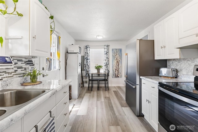 kitchen with light wood-style flooring, under cabinet range hood, backsplash, stainless steel appliances, and white cabinets