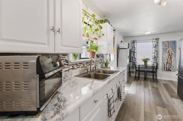 kitchen featuring backsplash, light countertops, light wood-type flooring, white cabinets, and a sink