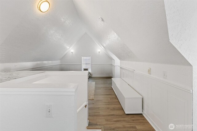 interior space featuring lofted ceiling, wood finished floors, a textured wall, and a textured ceiling