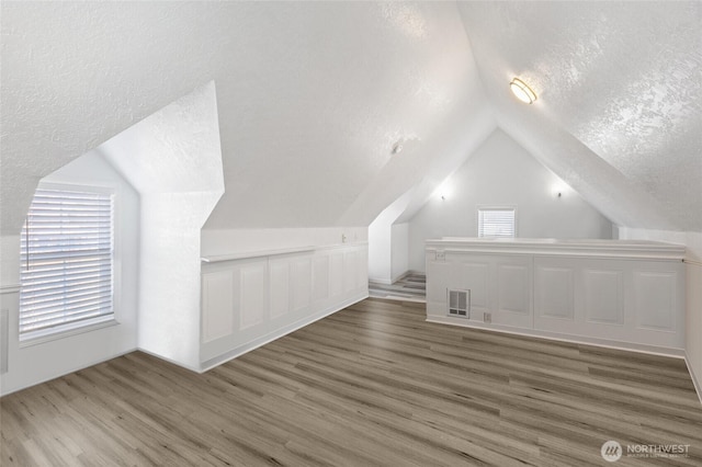 additional living space featuring lofted ceiling, wood finished floors, visible vents, and a textured ceiling