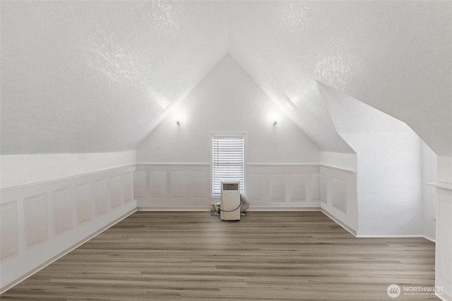 bonus room featuring lofted ceiling, wood finished floors, and a textured ceiling